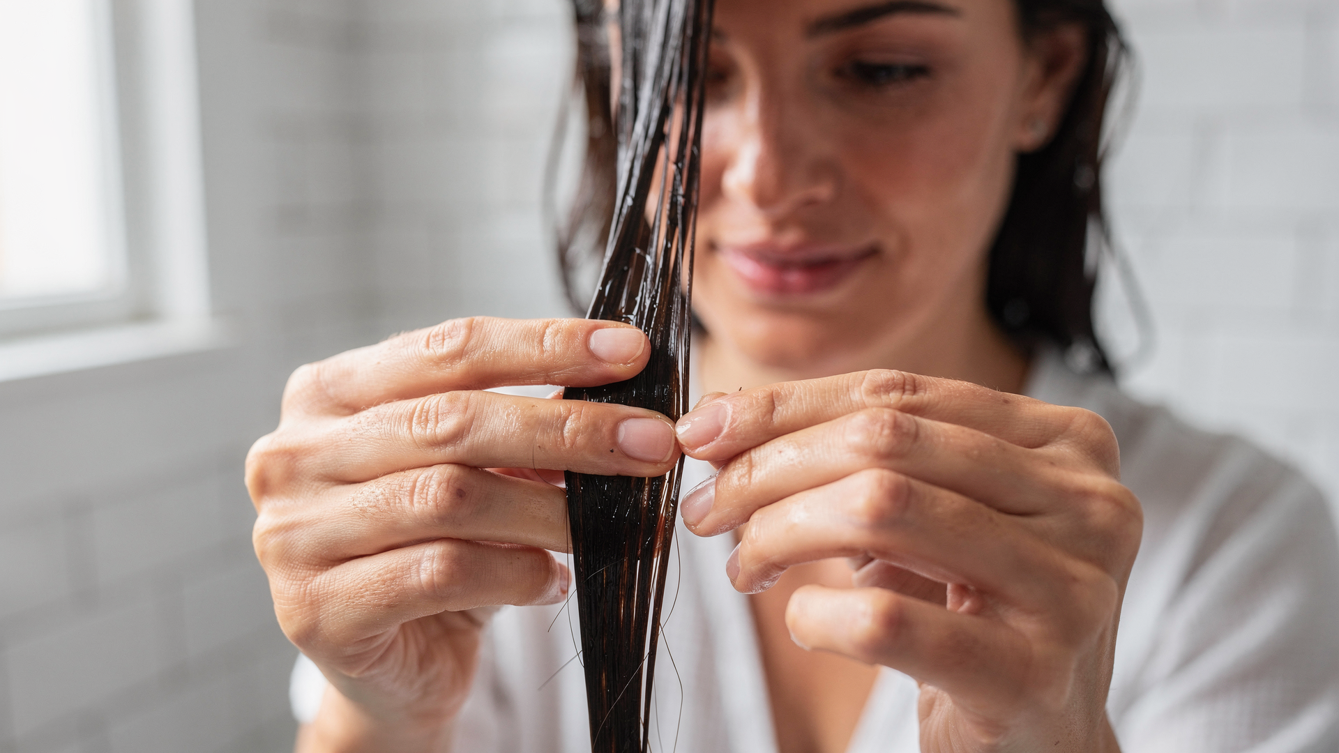 Mão esticando um fio de cabelo molhado para testar a elasticidade capilar