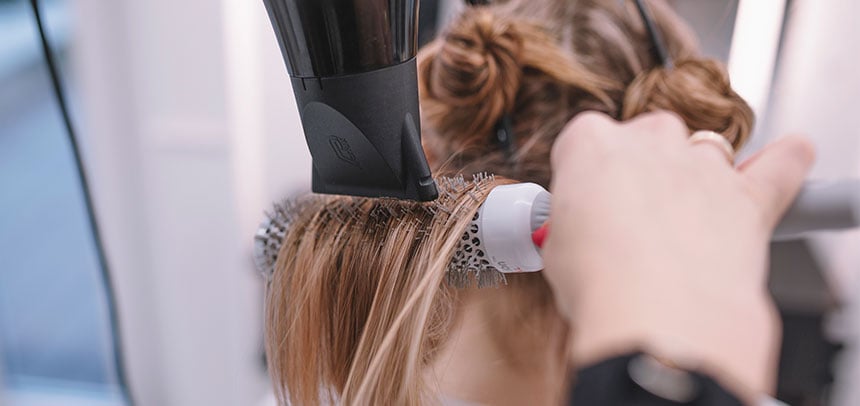 Mulher secando o cabelo com secador, aplicando protetor térmico antes